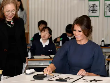 Ibu Negara AS Melania Trump bersiap menulis huruf kanji dengan bantuan siswa saat menghadiri kelas kaligrafi di sekolah dasar Kyobashi Tsukiji, Tokyo (6/11). Melania menulis karakter kaligrafi China dengan arti "Damai". (AFP Photo/Pool/Toshifumi Kitamura)