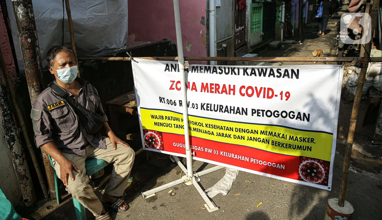 Seorang pria menjaga akses masuk zona merah COVID-19 di Kelurahan Petogogan RT 006 RW 003, Jakarta, Selasa (22/6/2021). Pemerintah Provinsi DKI Jakarta memperbarui data zona pengendalian virus Corona di tingkat rukun tetangga (RT) se-Ibu Kota.  (Liputan6.com/Faizal Fanani)