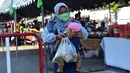 Seorang wanita yang mengenakan masker menggendong anaknya saat membeli makanan di pasar menjelang berbuka puasa selama bulan suci Ramadan di Provinsi Narathiwat, Thailand, Selasa (5/5/2020). Ramadan kali ini berlangsung di tengah bayang-bayang virus corona COVID-19. (Madaree TOHLALA/AFP)