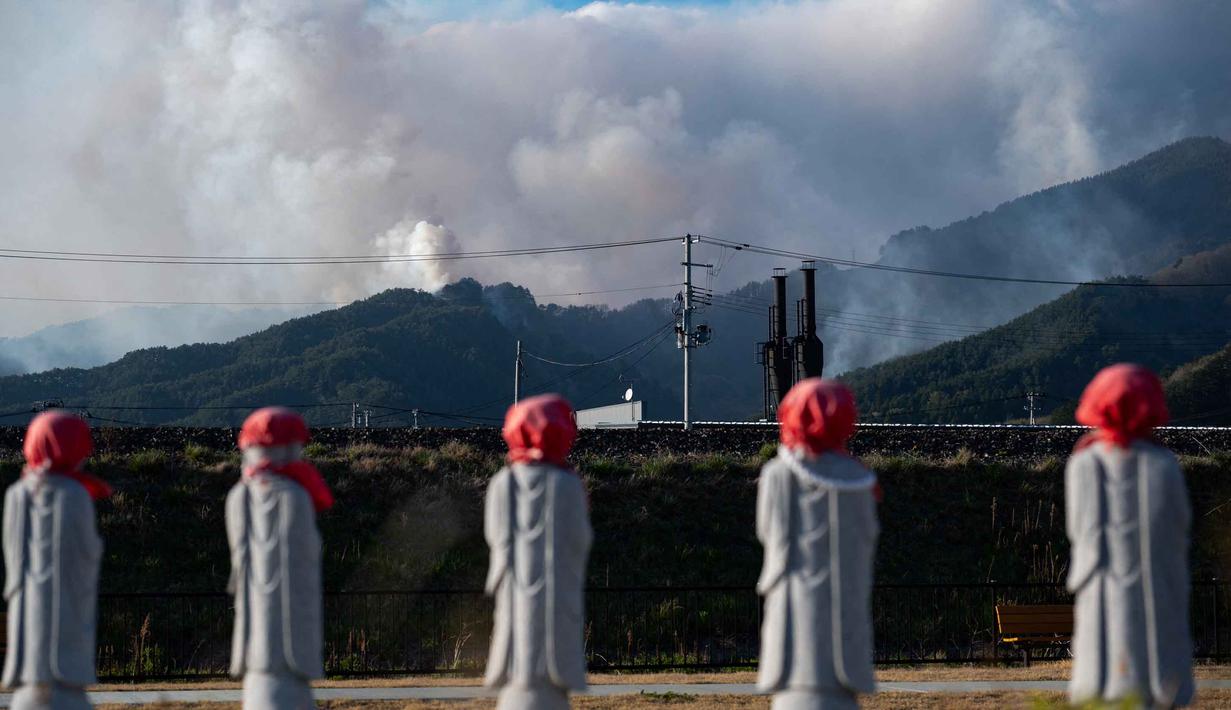 Cuaca kering memicu api cepat meluas, merusak beberapa bangunan dan menimbulkan perintah evakuasi bagi lebih dari 3.000 penduduk. Tampak dalam foto, patung-patung terlihat di sebuah taman sementara asap dari kebakaran hutan mengepul di latar belakang dekat kota Otsuchi, Prefektur Iwate, Jepang pada Sabtu 25 April 2026. (ANDREW CABALLERO-REYNOLDS/AFP)