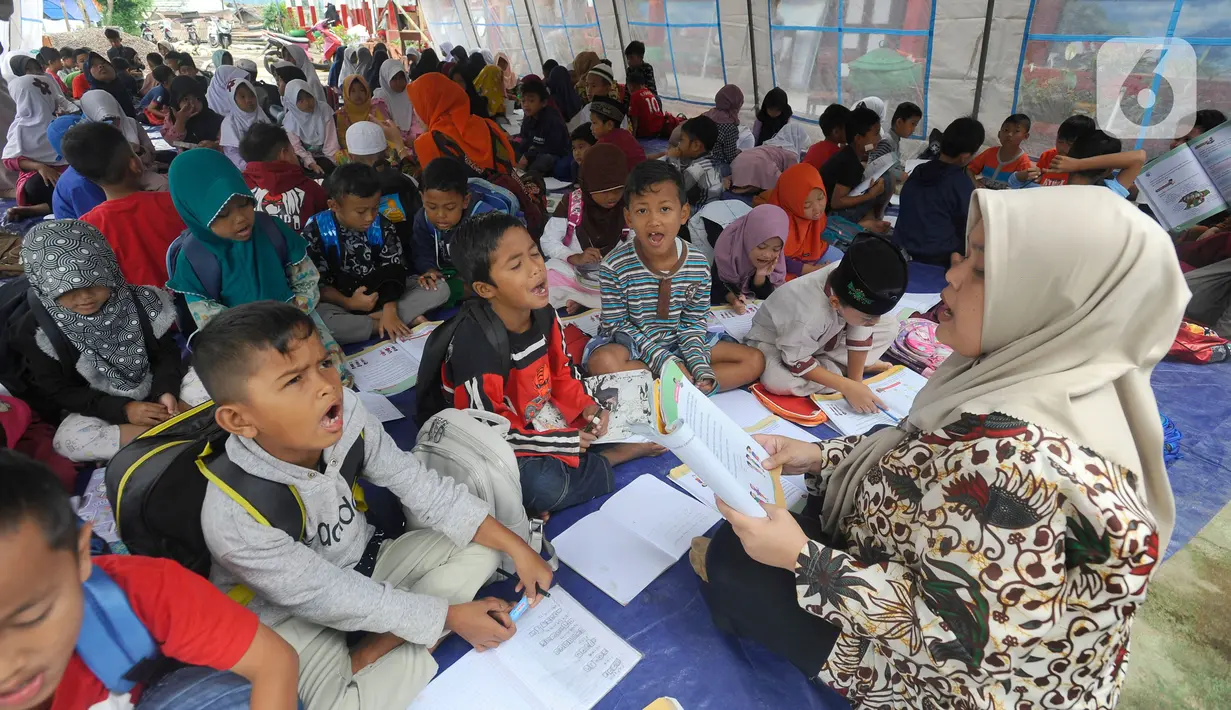 Guru mengajari murid-murid korban gempa belajar di dalam tenda darurat yang dibangun di halaman sekolah di SDN Gintung, Mangunkerta, Cianjur, Jumat (23/12/2022). Lebih dari sebulan sejak musibah gempa bumi 5,2 SR sejumlah murid sekolah di Cianjur masih belajar pada tenda darurat. (merdeka.com/Arie Basuki)