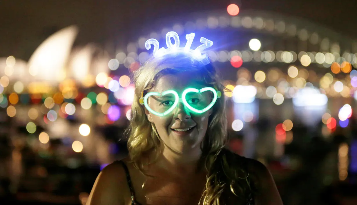 Pengunjung asal Inggris yang bernama Charlotte Kent memakai kacamata bercahaya dan atribut tahun baru saat menyaksikan pesta kembang api di Sydney Opera House dan Harbour Bridge, Sydney, Australia (31/12). (Reuters/Jason Reed)