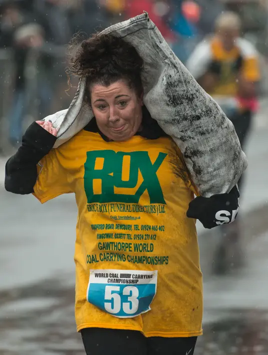 Seorang wanita membawa karung batu bara saat mengikuti World Coal Carrying Championships di Desa Gawthorpe, Wakefield, Inggris Utara, Senin (2/4). Peserta ditantang berlari sambil mengangkat karung batubara dengan jarak satu kilometer. (OLI SCARFF/AFP)
