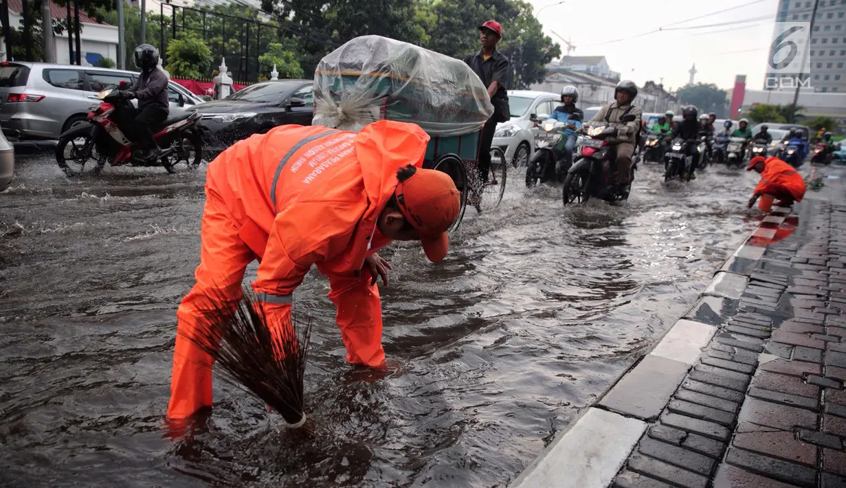 Petugas dari Dinas Kebersihan membuang genangan air kedalam selokan usai hujan deras dikawasan Tugu Tani, Jakarta, Kamis (12/10). Tingginya curah hujan membuat genangan disisi jalan. (Liputan6.com/Faizal Fanani)