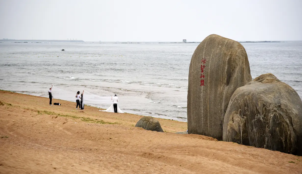 Sepasang pengantin berpose untuk foto pernikahan di sebuah pantai di Rizhao, Provinsi Shandong, China timur (9/7/2020). (Xinhua/Wang Kai)