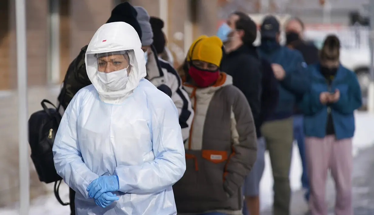 Petugas pengujian COVID-19 Departemen Kesehatan Salt Lake County berjalan melewati antrean warga di luar Departemen Kesehatan Salt Lake County, Salt Lake City, Utah, Amerika Serikat, 28 Desember 2021. Saham maskapai-maskapai AS anjlok akibat lonjakan kasus COVID-19. (AP Photo/Rick Bowmer)