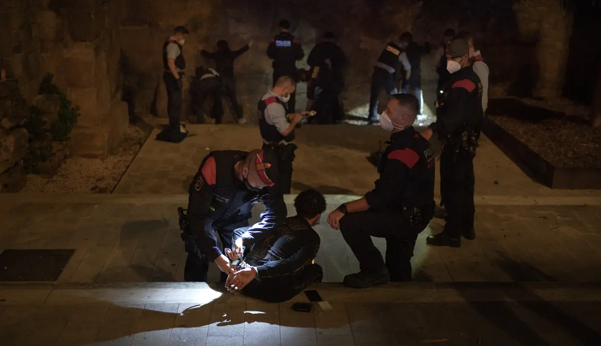 Orang-orang ditahan dan diperiksa Mossos d'Escuadra, kepolisian regional Catalonia, setelah jam malam di Barcelona pada 1 November 2020. Pemerintah Spanyol menetapkan pembatasan gerak atau jam malam yang berlaku pukul 22.00 untuk mengendalikan lonjakan kasus Covid-19. (AP Photo/Emilio Morenatti)