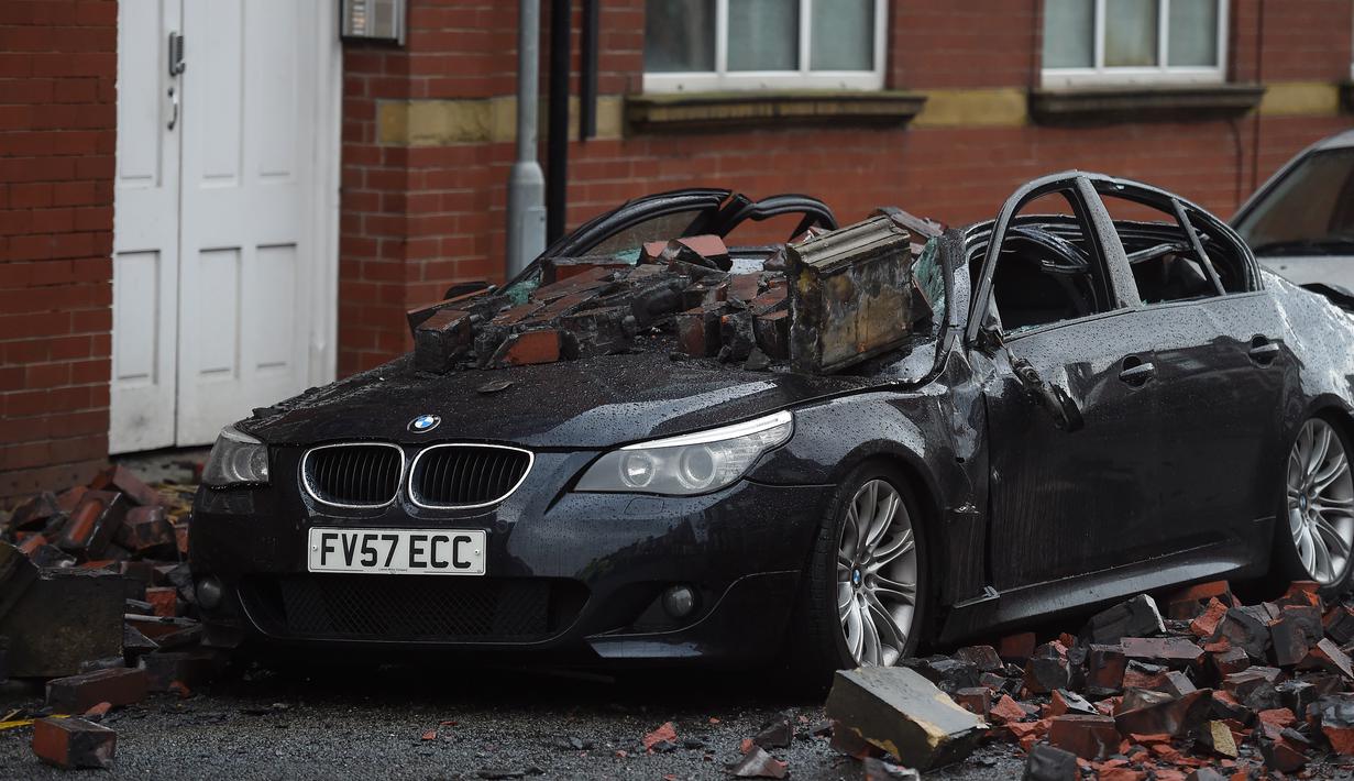 Reruntuhan atap apartemen tampak menimpa sebuah mobil yang diparkir akibat angin kencang yang melanda di Leigh, barat laut Inggris, Rabu (18/11). (AFP PHOTO/Paul Ellis)