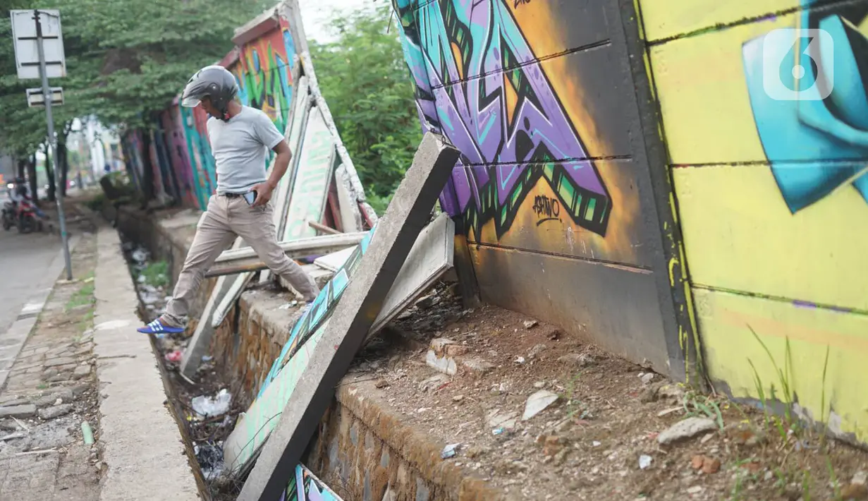 Seorang  pria melintas dekat tembok Jalan Juanda yang ambruk di kawasan Depok, Jawa Barat, Senin (2/12/2019). Kondisi tembok yang dipenuhi mural tersebut mulai rapuh dan sebagian sisinya telah ambruk serta miring sehingga membahayakan pejalan kaki. (Liputan6.com/Immanuel Antonius)