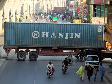 Sejumlah pengendara motor melewati kolong sebuah truk kontainer di Rawalpindi, Pakistan (28/10). Kejadian ini akibat sejumlah truk kontainer memblokir jalan raya selama demo yang digelar Awami Muslim League (AML). (Reuters/Faisal Mahmood)