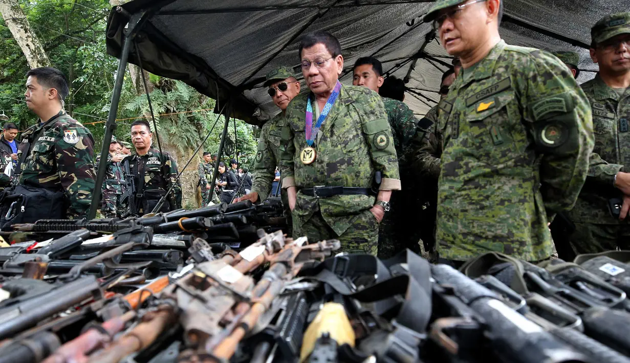 Presiden Filipina, Rodrigo Duterte meninjau ratusan pucuk senjata yang berhasil disita oleh tentara Filipina sejak konflik di Marawi, Kamis (20/7). Duterte melakukan kunjungan mendadak ke medan pertempuran dengan terbang menumpang helikopter (AP Photo)
