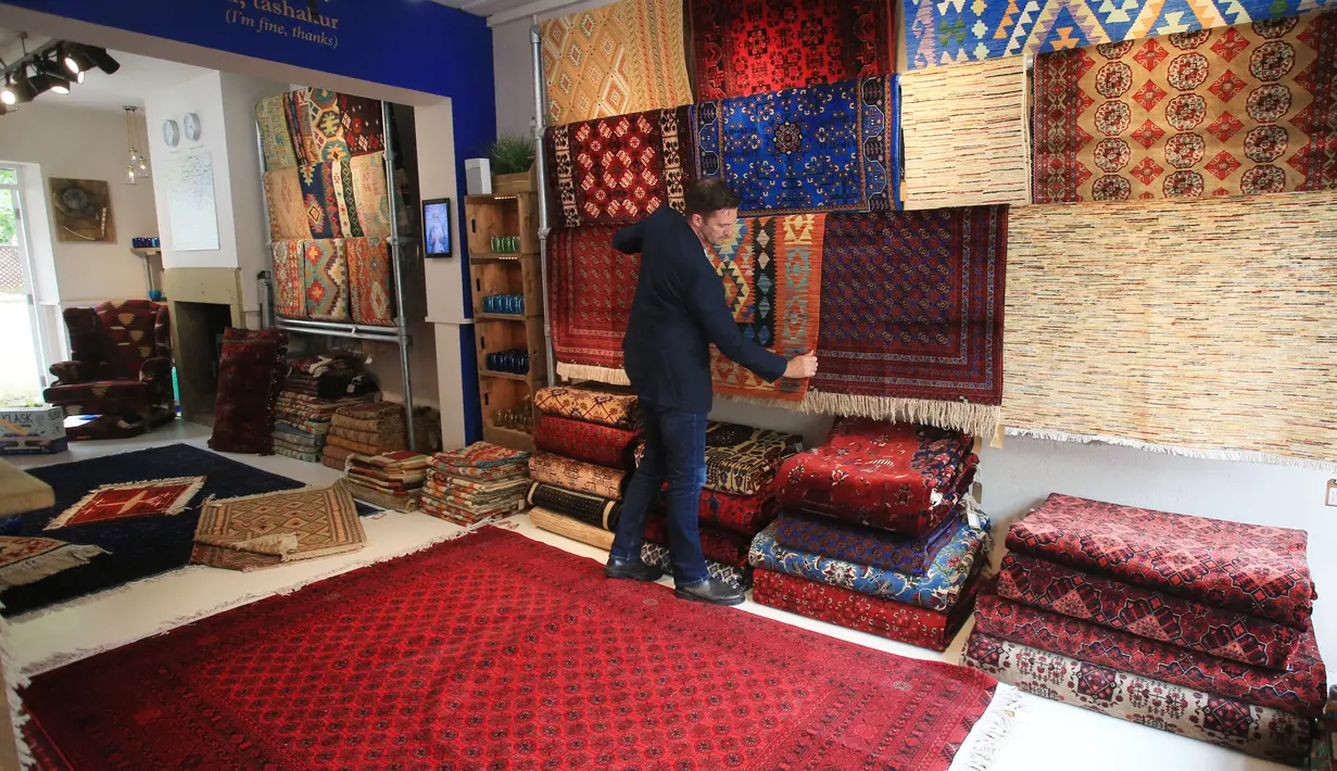 Pemilik The Afghan Rug Shop James Wilthew mengatur pajangan di tokonya di Hebden Bridge, Inggris, 20 Agustus 2021. Menurut mantan prajurit itu ada sekitar 200 keluarga yang didukung oleh perusahaannya, The Afghan Rug Shop. (LINDSEY PARNABY/AFP)