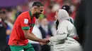 <p>Gelandang Maroko #17 Sofiane Boufal merayakan bersama ibunya setelah lolos ke semifinal dengan mengalahkan Portugal pada babak 8 besar Piala Dunia 2022 di Stadion Al-Thumama di Doha, Sabtu (10/12/2022). Pemain klub Prancis, Angers, itu berputar-putar berbagi kebahagiaan dengan keluarga. (KARIM JAAFAR / AFP)</p>