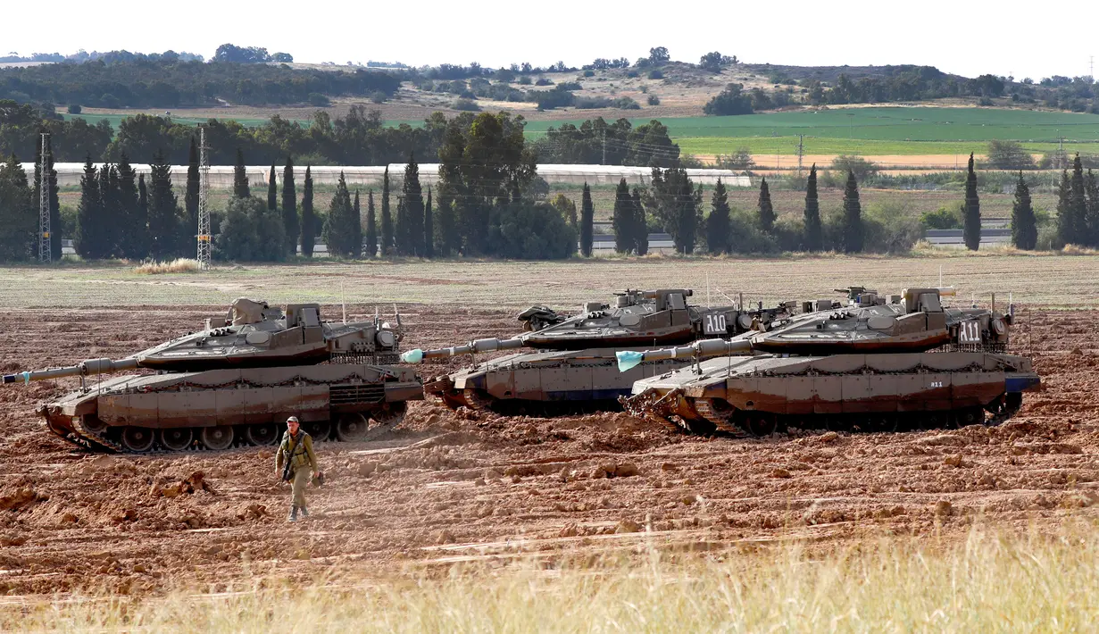 Seorang tentara Israel berjalan melewati tank Merkava yang terparkir di dekat perbatasan dengan Jalur Gaza, Israel, Senin (6/5/2019). Para pemimpin Palestina di Gaza menyetujui gencatan senjata dengan Israel. (JACK GUEZ/AFP)