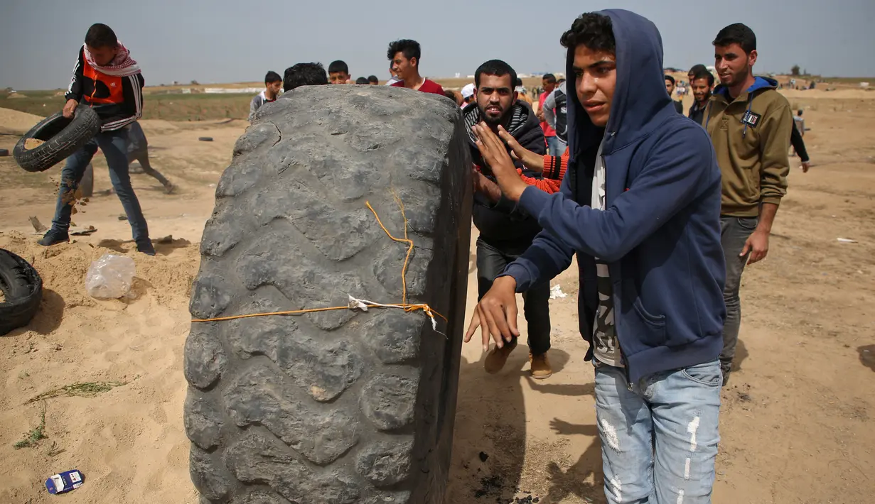 Pemuda Palestina membawa ban untuk dibakar saat menggelar aksi di perbatasan Palestina-Israel di kota Gaza tengah (13/4). Hal tersebut merupakan unjuk rasa ketiga menyusul tewasnya 33 orang Palestina akibat serangan tentara Israel. (AFP/Mohammed Abed)