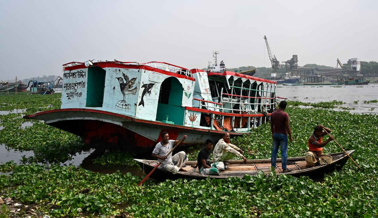 Orang-orang menonton feri yang diselamatkan setelah kecelakaan di Sungai Shitalakshya di Narayanganj, Bangladesh (21/3/2022). Feri ML Afsar Uddin tenggelam di sungai setelah ditabrak kapal kargo. (AFP/Munir uz Zaman)