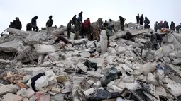 Warga dan tim penyelamat mencari korban dan orang yang selamat di antara puing-puing bangunan yang runtuh setelah gempa bumi di desa Besnaya, provinsi Idlib Barat Laut Suriah perbatasan dengan Turki, pada Senin 6 Februari 2022. Tim penyelamat di Turki dan Suriah menerjang cuaca yang sangat dingin, gempa susulan, dan bangunan yang runtuh, saat mereka menggali korban yang tertimbun oleh gempa bumi yang menewaskan lebih dari 5.000 orang. (OMAR HAJ KADOUR/AFP)
