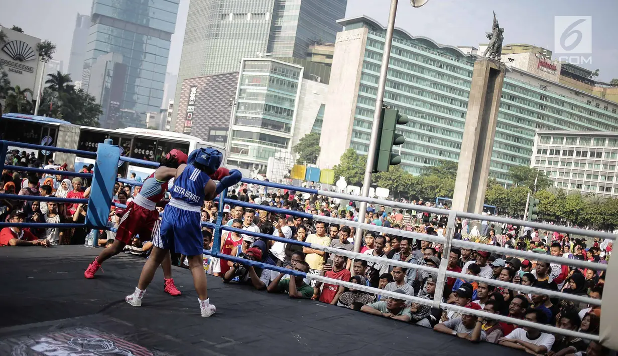 Warga menyaksikan pertandingan tinju amatir yang berlangsung saat Car Free Day di kawasan Bundaran HI, Jakarta, Minggu (29/4). Pertandingan tersebut untuk mendukung penyelenggaraan Asian Games 2018. (Liputan6.com/Faizal Fanani)
