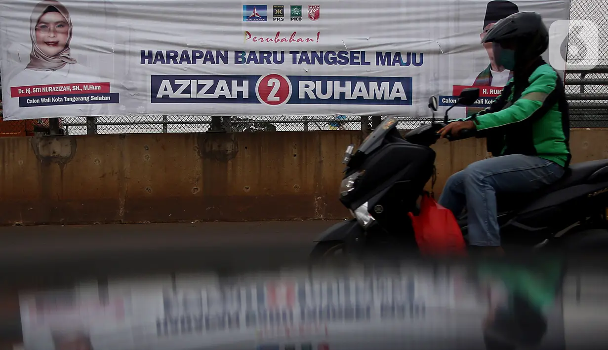 Pengedara melintas di depan alat peraga kampanye (APK) yang terpasang di kawasan Depok, dan Ciputat, Tangerang Selatan, Minggu (18/10/2020). KPU Kota Tangsel dan Depok membagikan sejumlah alat peraga kampanye kepada pasangan calon Pilkada 2020 serentak. (Liputan6.com/Johan Tallo)