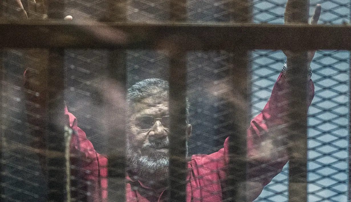 Mantan Presiden Mesir Mohammed Morsi mengenakan seragam merah saat menjalani sidang di Kairo, Mesir, 23 April 2016. Mohammed Morsi tiba-tiba pingsan dan kemudian meninggal saat menjalani sidang pengadilan pada Senin 17 Juni 2019 waktu setempat. (KHALED DESOUKI/AFP)