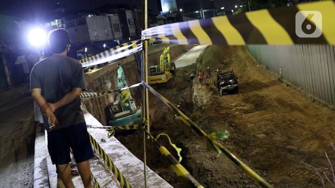 Warga menyaksikan pengerjaan proyek underpass Senen Extension, Jakarta, Minggu (3/5/2020). Meski dalam penerapan Pembatasan Sosial Berskala Besar (PSBB) akibat pandemi COVID-19, pengerjaan proyek yang ditargetkan selesai pada Desember 2020 tetap berjalan. (Liputan6.com/Helmi Fithriansyah)