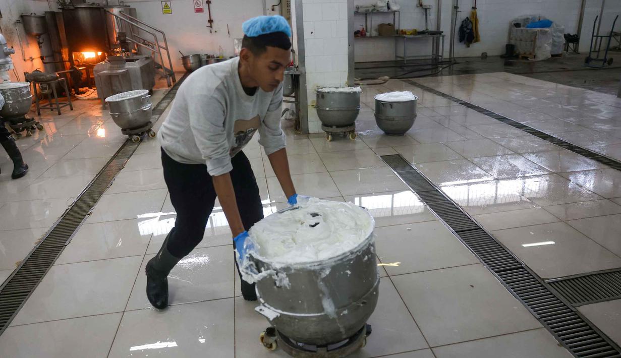 Saat ini, pabrik beroperasi dengan kapasitas yang masih disesuaikan. Tampak dalam foto, seorang karyawan Palestina memindahkan sebuah wadah berisi isian kue manis yang dikenal secara lokal sebagai "al-Shatwi" (kue musim dingin) Crimbo, saat pabrik Al-Arees secara bertahap melanjutkan produksinya setelah terhenti akibat perang, di Deir al-Balah, Jalur Gaza tengah pada 12 Januari 2026, (Bashar Taleb/AFP)