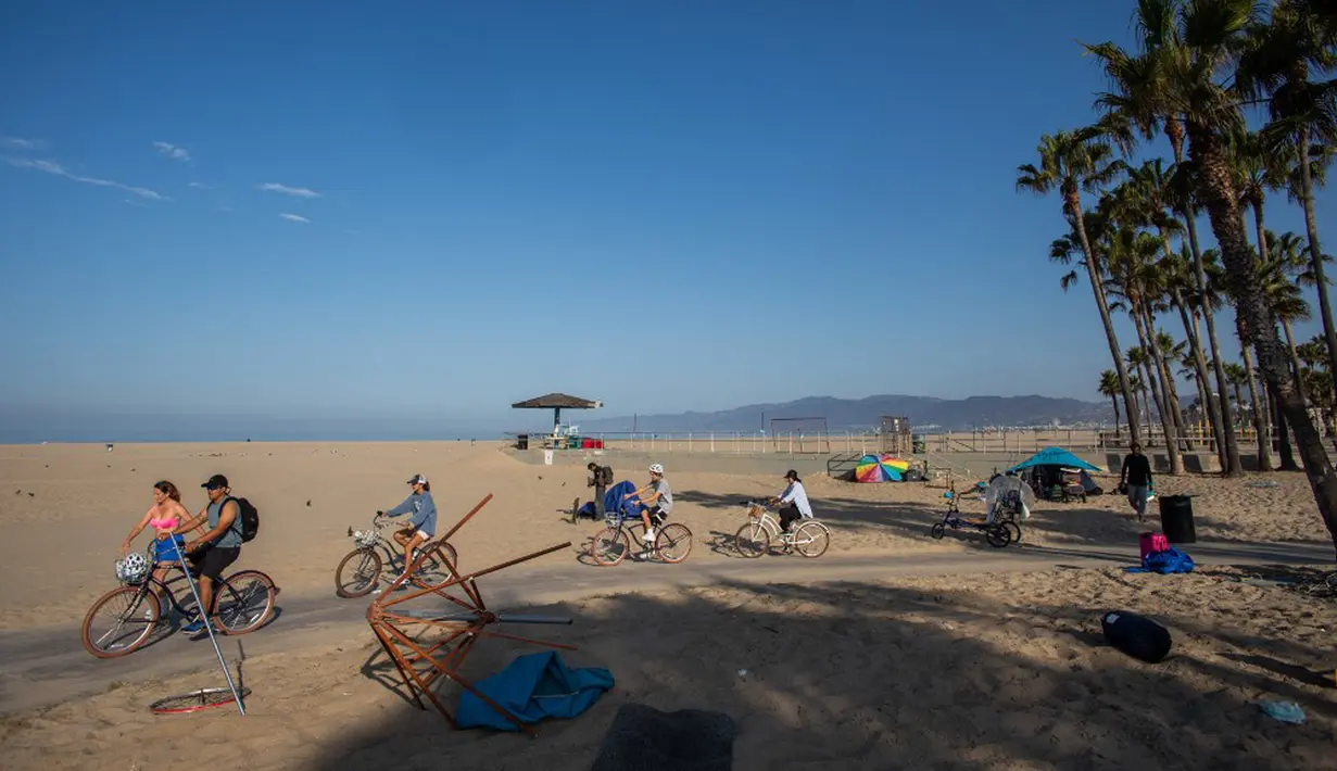Orang-orang mengendarai sepeda sementara tenda tunawisma terlihat pada latar belakang di Venesia, California, Amerika Seikat, 12 Agustus 2021. (Apu GOMES/AFP)