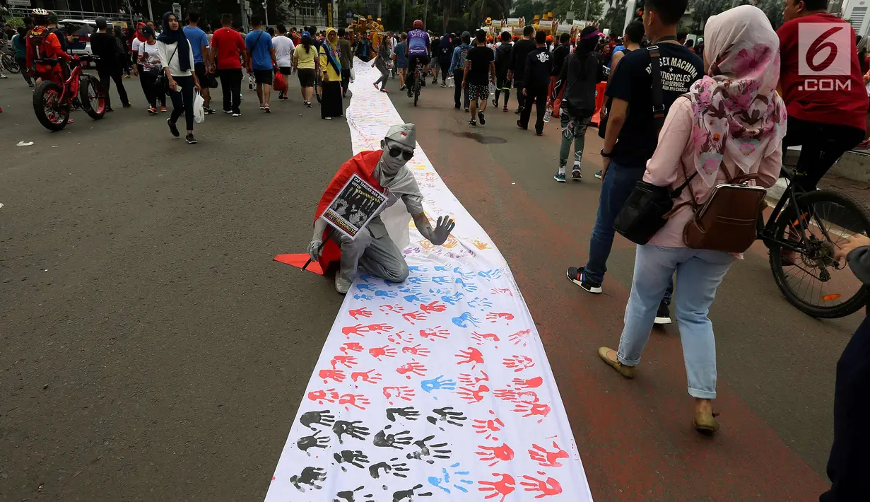Warga berpose di dekat spanduk sepanjang satu kilometer bekas Cap tangan anak-anak Indonesia, di Kawasan Car Free Day, Jakarta (24/9). Spanduk tersebut untuk menunjukkan dukungan kepada Etnis minoritas Rohingya di Myanmar. (Liputan6.com/Johan Tallo)