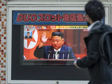 Seorang pria melewati layar televisi yang menampilkan laporan berita tentang peluncuran rudal terbaru Korea Utara dengan gambar pemimpin Korea Utara, Kim Jong Un, di sepanjang jalur pejalan kaki di Tokyo, Kamis (3/11/2022). Korea Utara kembali luncurkan tiga rudal pada Kamis pagi dan salah satu di antaranya terbang di atas Jepang. (Photo by Richard A. Brooks / AFP)