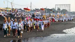 Melasti merupakan upacara adat yang bertujuan untuk menyucikan diri dan membersihkan alam dari energi negatif. Tampak dalam foto, umat Hindu saat mengikuti upacara doa Melasti di salah satu pantai di Denpasar, Bali, pada Senin 16 Maret 2026. (SONNY TUMBELAKA/AFP)