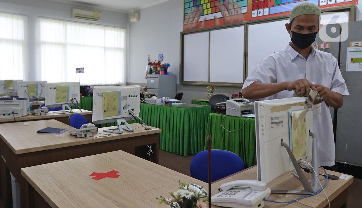 Petugas sekolah sedang membersihkan komputer sebelom murid-murid melakukan pelajaran di  SMKN 51, Jakarta, Rabu (7/4/2021). SMKN 51 melakukan uji coba masuk sekolah dan Uji Sertifikasi Kompetensi (USK) dengan protokol kesehatan yang ketat. (Liputan6.com/Herman Zakharia)