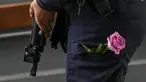 Seorang petugas polisi berjaga dengan bunga di sakunya saat orang-orang berkumpul untuk mengenang para korban di pintu masuk pusat perbelanjaan Field di Kopenhagen, Denmark, 5 Juli 2022. Polisi mengatakan seorang pria bersenjata yang membunuh tiga orang ketika dia melepaskan tembakan di pusat perbelanjaan yang ramai bertindak sendiri dan tampaknya memilih korbannya secara acak. (AP Photo/Sergei Grits)