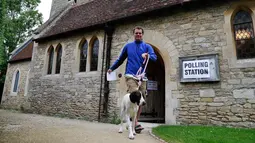 Seorang pria bersama anjingnya meninggalkan gereja yang dijadikan tempat pemungutan suara pemilu parlemen Inggris di Stadhampton, Kamis (8/6). Para pemilih mengajak anjingnya untuk menemani mereka mengambil bagian dalam Pemilu Inggris. (Adrian DENNIS/AFP)
