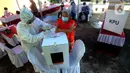 Petugas Kelompok Penyelenggara Pemungutan Suara (KPPS) dengan memakai baju hazmat membantu pemilih memasukkan kertas suara usai menggunakan hak pilihnya dalam Pilkada Tangerang Selatan 2020 di TPS 46, Paku Jaya, Serpong Utara, Rabu (9/12/2020). (merdeka.com/Arie Basuki)
