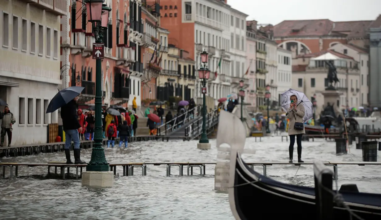 Seorang wanita mengambil gambar dari atas papan saat gelombang pasang menerjang Venesia, Italia, Selasa (12/11/2019). Venesia dilanda banjir akibat gelombang pasang setinggi 127 cm. (AP Photo/Luca Bruno)
