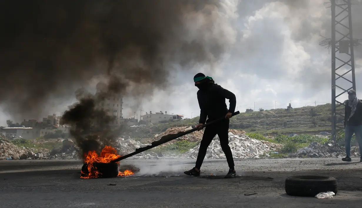Pengunjuk rasa Palestina membakar ban saat bentrokan dengan pasukan Israel di pinggiran Kota Ramallah, Tepi Barat, Rabu (27/3). Bentrokan ini sebagai bentuk protes terhadap tahanan Palestina yang berada di Israel. (AP Photo/Majdi Mohammed)