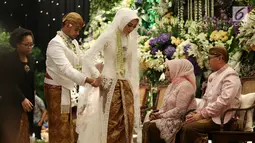 Putra Ketua MPR, Ray Zulham Farras Nugraha merapihkan busana sang istri DR. Milka Anisya Norosiya saat acara pernikahan di Jakarta, Minggu (24/9). Acara pernikahan tersebut di hadiri beberapa Tokoh dan Pejabat Publik. (Liputan6.com/Johan Tallo)