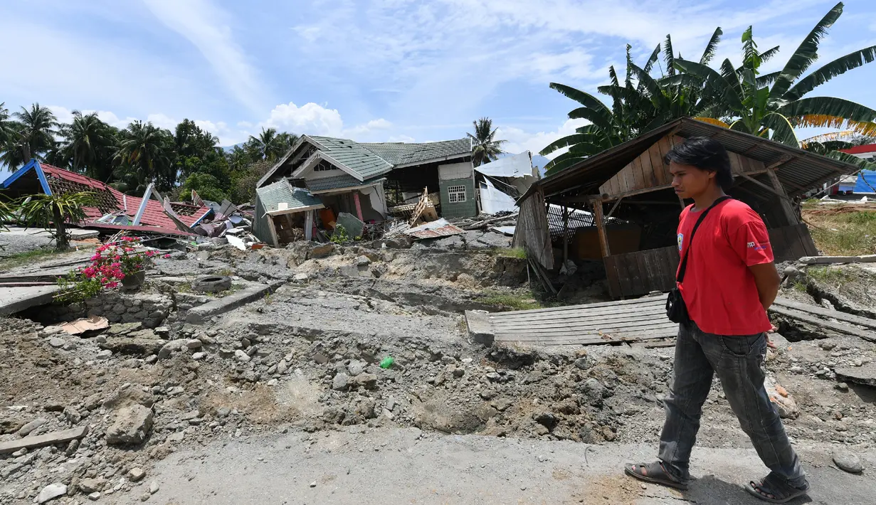Seorang pria berjalan melewati jalan rusak usai gempa dan tsunami melanda Kabupaten Sigi, Sulawesi Tengah, Kamis (4/10). BNPB mengatakan ada empat kecamatan sulit dijangkau petugas usai gempa dan tsunami melanda daerah tersebut. (ADEK BERRY/AFP)
