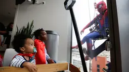 Pasien anak mengamati superhero Spiderman membersihkan kaca jendela kamar sebuah rumah sakit di Birmingham, Rabu (11/10). Sekelompok superhero bekerja membersihkan jendela rumah sakit untuk menghibur anak- anak yang sedang sakit. (AP Photo/Brynn Anderson)