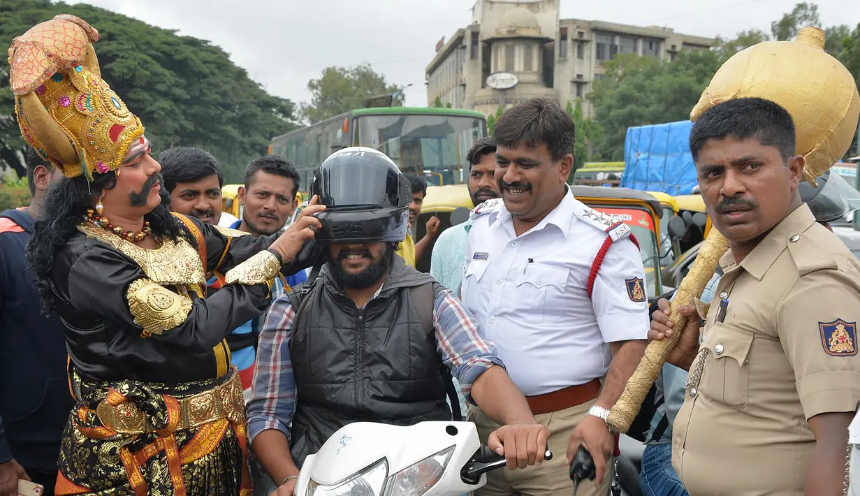 Seorang seniman berpakaian seperti "Yamaraj" (R), dewa kematian Hindu, memakaikan helm kepada pengendara motor saat  kampanye 'Road Safety Week' di Bangalore (10/7). (AFP Photo/Manjunath Kiran)