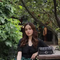 Syifa Hadju duduk di sebuah taman dengan menampilkan Tabby Shoulder Bag 20 Coach (Foto Dok: KANMO GROUP).