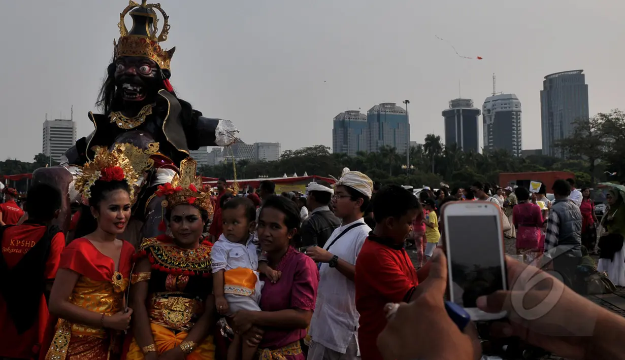Sejumlah warga berfoto di dekat boneka raksasa saat pawai Ogoh-ogoh di kawasan Monas, Jakarta, Jumat (20/3/2015). Pawai tersebut merupakan rangkaian dari prosesi menjelang Hari raya Nyepi Tahun Saka 1937. (Liputan6.com/Johan Tallo) 