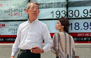 Orang-orang berjalan melewati sebuah indikator saham elektronik sebuah perusahaan sekuritas di Tokyo (29/8). Bursa saham Asia turun setelah Korea Utara (Korut) melepaskan rudalnya ke Samudera Pasifik. (AP Photo/Shizuo Kambayashi)