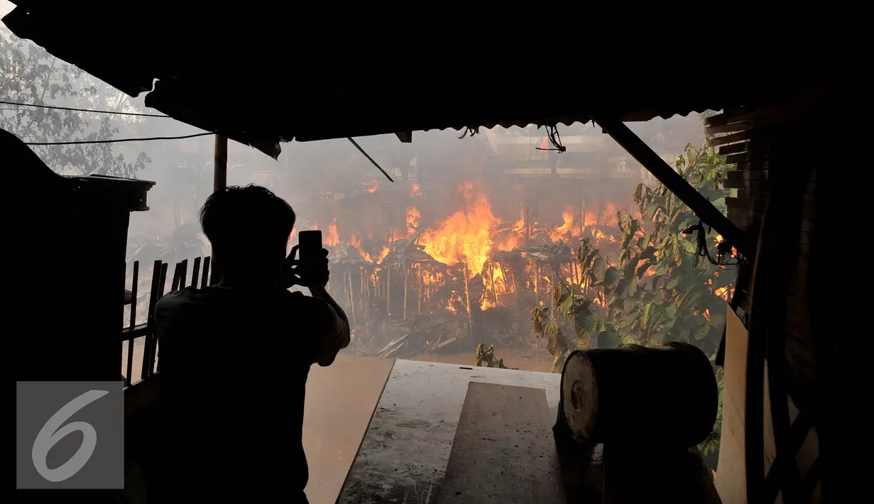 Seorang warga mengabadikan gambar saat terjadinya kebakaran yang melanda rumah hunian semi permanen di bantaran sungai anak kali ciliwung, Kawasan Kampung Berland, Jakarta, Rabu (2/9/2015). (Liputan6.com/Johan Tallo)