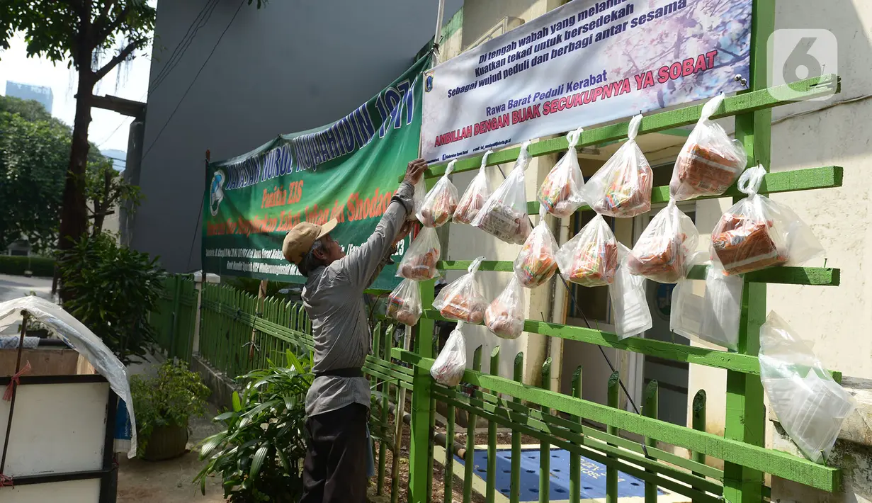 Pedagang mengambil sembako yang digantung di rak kayu sisi jalan di kawasan Rawa Barat, Jakarta Selatan, Kamis (14/5/2020). Selama masa pandemi COVID-19, pihak kelurahan dan masjid sekitar menyediakan paket berisi mi instan, telur, dan masker untuk warga yang membutuhan. (merdeka.com/Imam Buhori)