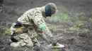 Seorang pencari ranjau dari Kementerian Dalam Negeri Ukraina menjinakkan ranjau pada ladang ranjau setelah pertempuran baru-baru ini di Irpin dekat Kiev, Ukraina, 19 April 2022. (AP Photo/Efrem Lukatsky)