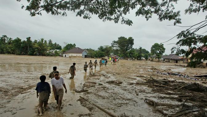Penduduk desa berjalan melalui daerah banjir di desa Radda di Kabupaten Luwu Utara, Sulawesi Selatan (14/7/2020). Akibat musibah banjir bandang ini setidaknya sekitar 15 orang tewas dan belasan lainnya dinyatakan hilang. (AP Photo)