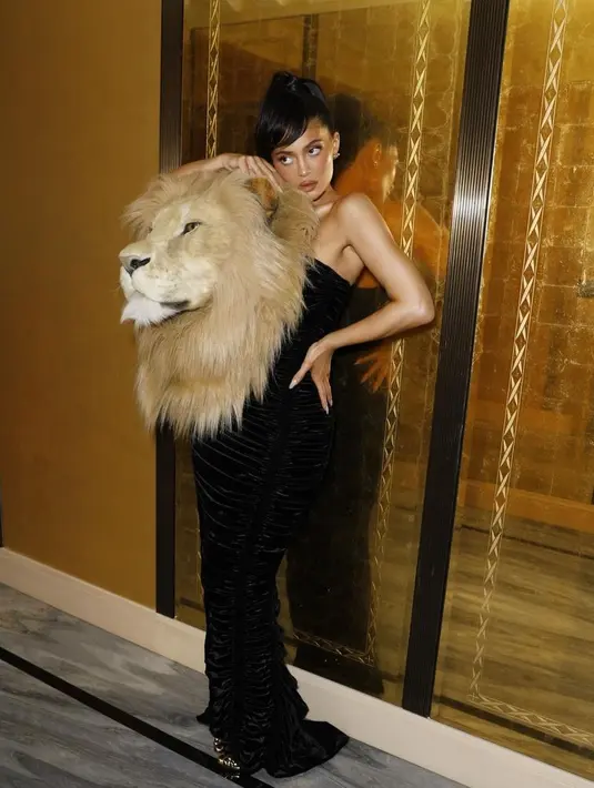 Kylie Jenner tiba menggunakan gaun strapless beludru hitam Schiaparelli SS23, berhiaskan kepala singa berukuran aslinya. [@schiaparelli].