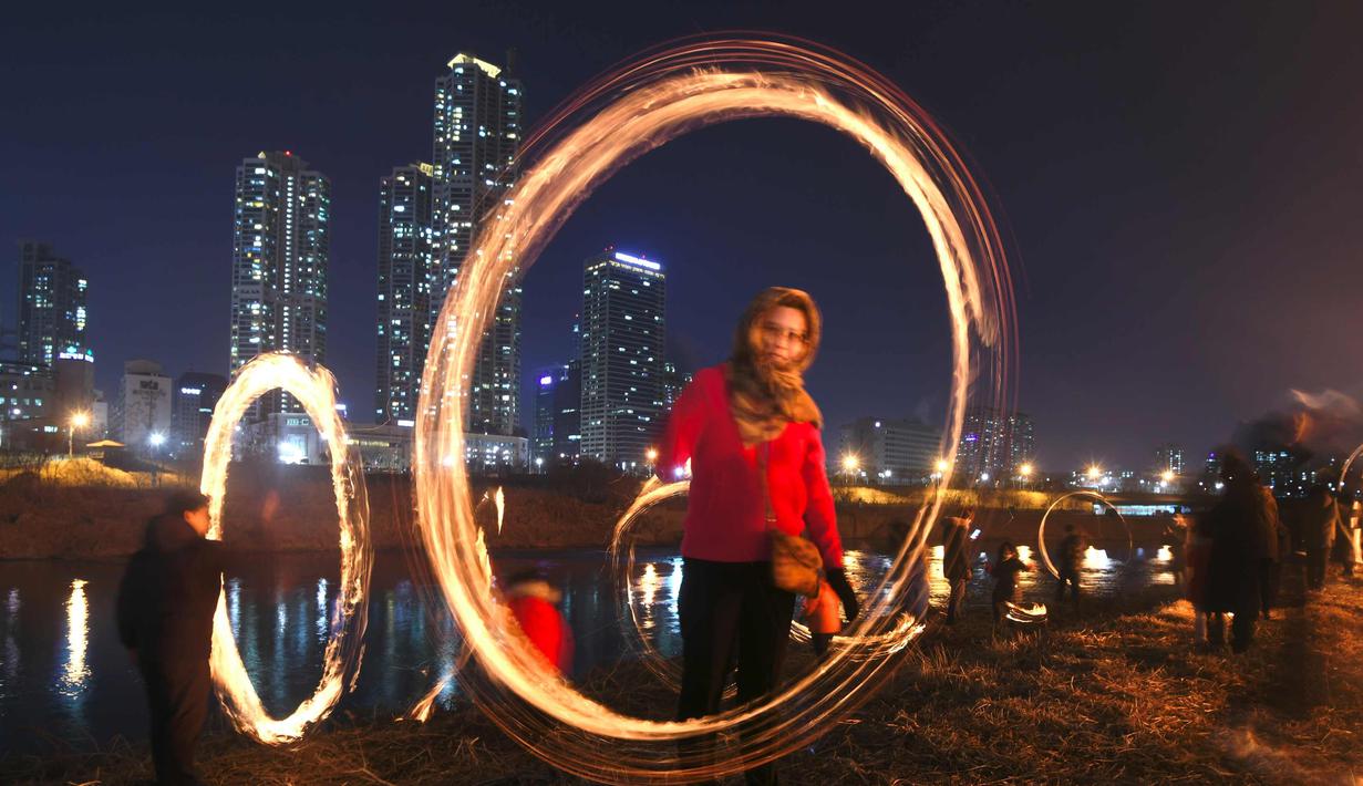 Peserta memutar kaleng arang yang terbakar menjelang perayaan "Jeongwol Daeboreum" (Bulan Purnama) di sebuah taman di Seoul, Korea Selatan (1/3). Permainan ini dipercaya dapat menyuburkan tanah dan menyingkirkannya hama. (AFP Photo/Jung Yeon-je)
