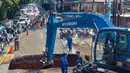 Para pengendara melintas di jalan yang padat sementara para pekerja menggunakan alat berat membersihkan puing-puing dari lubang runtuhan yang terbentuk di Jalan Raya Lenteng Agung (arah Depok), Jakarta pada Jumat 29 Mei 2026. (BAY ISMOYO/AFP)